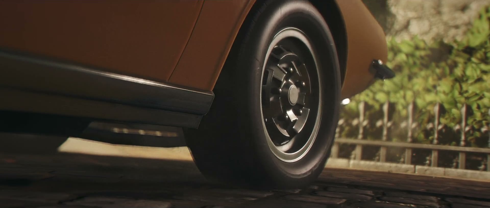 Official 007 First Light screenshot — a low-angle view of a classic sports car's wire wheel as it powers along a road.