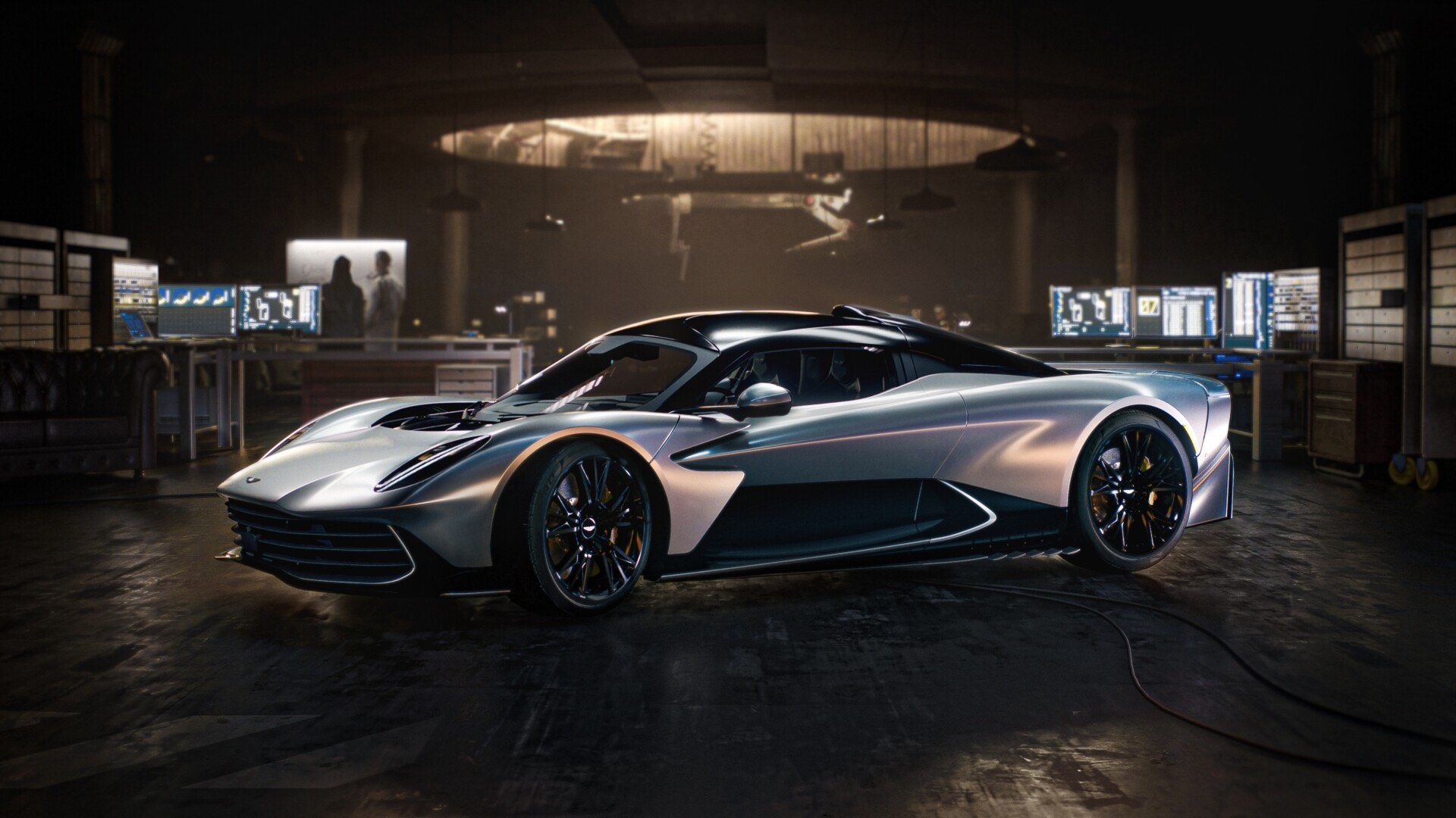 A sleek silver sports car parked in a dimly lit workshop lined with monitors in 007 First Light.