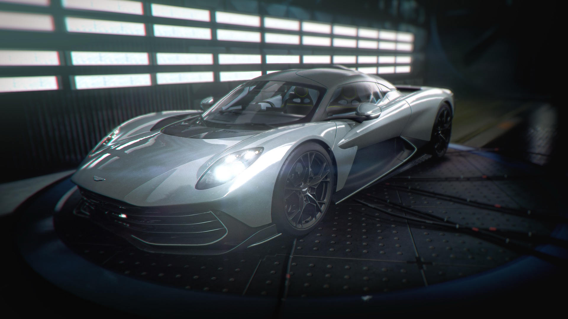Official 007 First Light screenshot — a silver Aston Martin Valhalla on a lit workshop turntable in a dark garage.